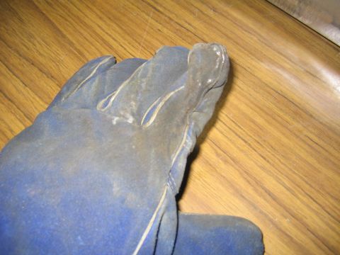 1978 Ford Bronco - A worn, faded blue leather work glove lies on a wood-grain surface, showing dirt and wear on the fingers and thumb.