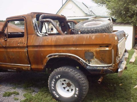 1988 Ford Bronco - This heavily rusted Ford Bronco shows its rear quarter and spare tire, with white spoke wheels.