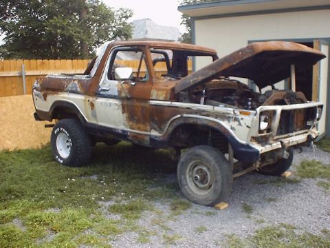 1988 Ford Bronco - This heavily rusted Ford Bronco, likely from the late 1970s, sits with its hood ajar, revealing its engine bay.