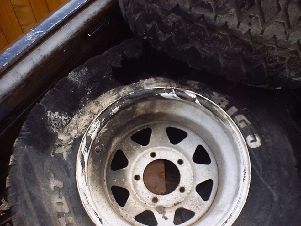 Spare tire with white-lettered sidewall and a silver 5-spoke wheel, dirty and worn