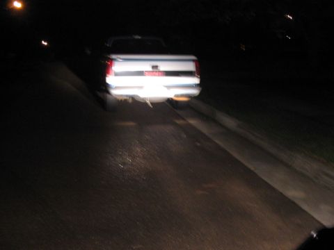 1988 Ford Bronco - A white pickup truck is seen from the rear at night on a road.