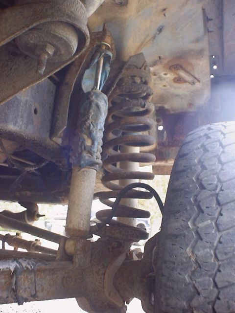 1988 Ford Bronco - Detail shot of the suspension system, showing a coil spring and shock absorber, with a tire visible on the right.