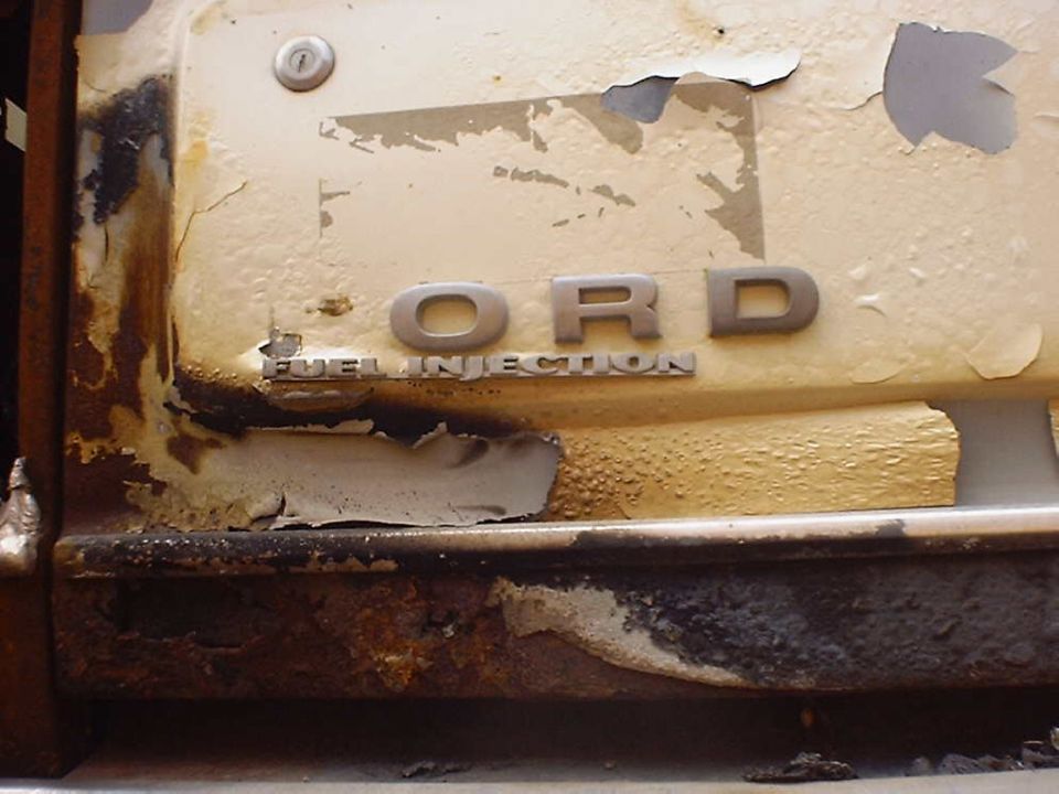 Close-up of a rusty Ford emblem and 'FUEL INJECTION' badge on a vehicle