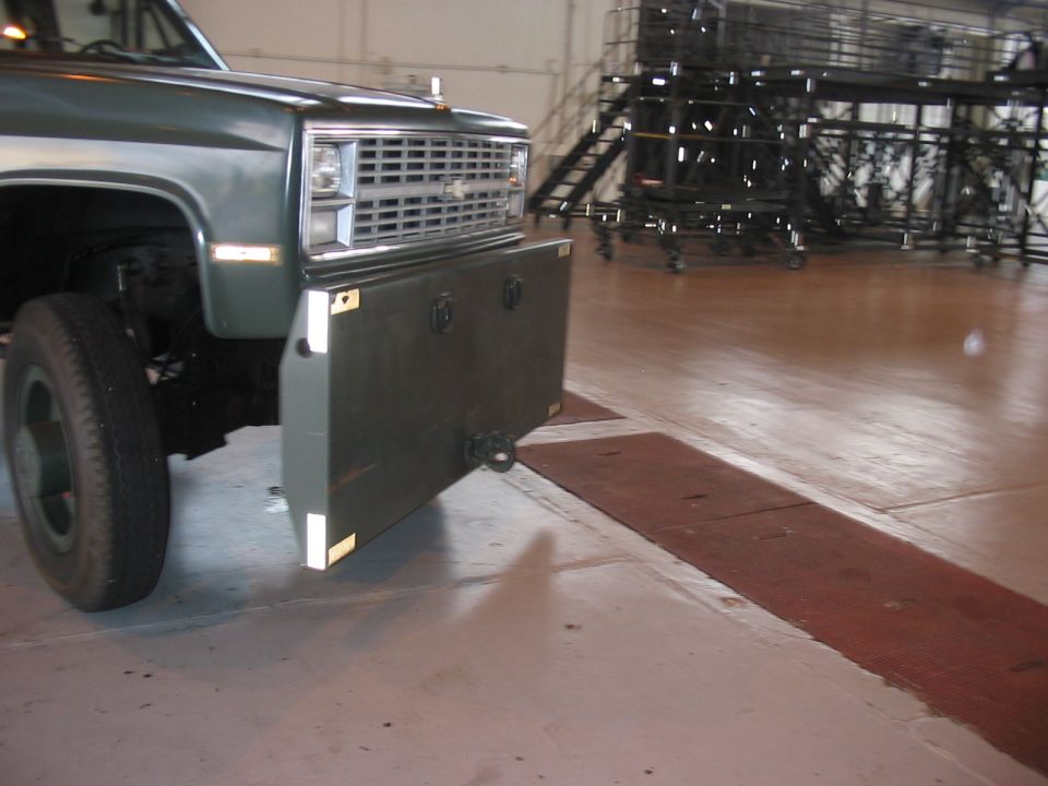 Front of a dark green truck with a large, flat, dark bumper attached. Grille is visible