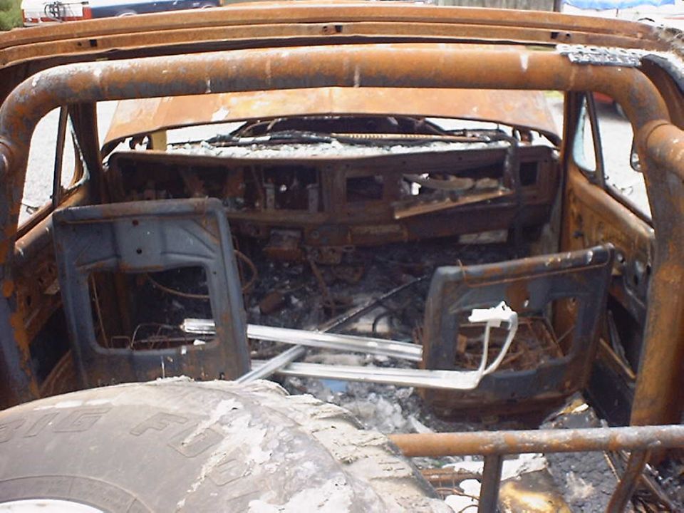 Burnt-out interior of a 1978 Ford Bronco with a roll cage, showing melted dashboard and seats