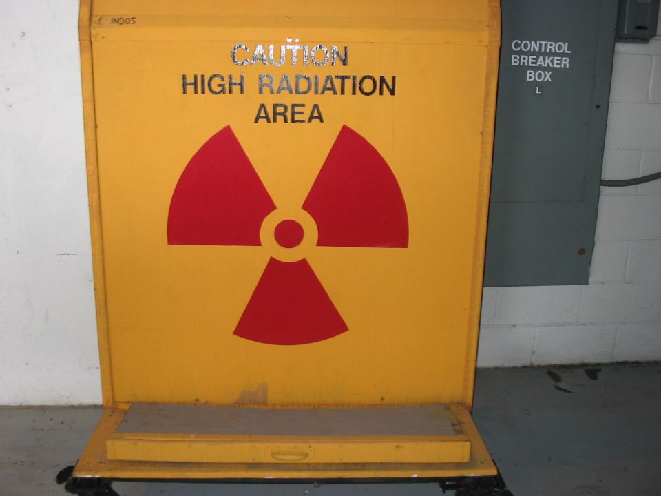 Yellow sign with red radiation symbol and text 'CAUTION HIGH RADIATION AREA'. Gray electrical box on right