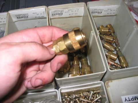 1988 Ford Bronco - A hand holds a brass quick connect fitting over bins containing more fittings and screws.