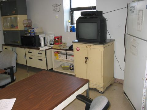 1988 Ford Bronco - An office breakroom scene features a television set atop a cabinet, alongside a refrigerator and various office appliances.