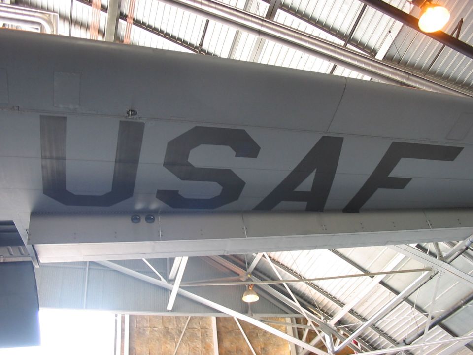Close-up of large "USAF" text on the side of a gray aircraft fuselage inside a hangar