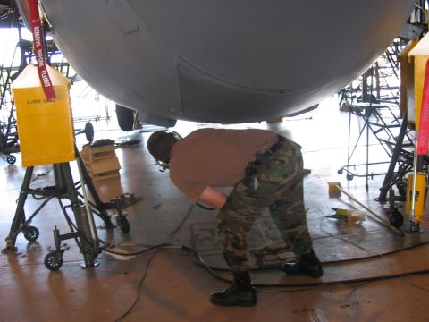 1988 Ford Bronco - A person works on the underside of a large aircraft in a hangar, with maintenance equipment nearby.