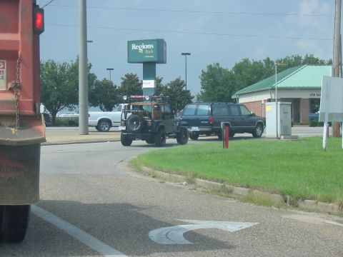 1988 Ford Bronco - A dark green Jeep Wrangler is seen from behind, towing a trailer, with a blue SUV and white pickup truck nearby.