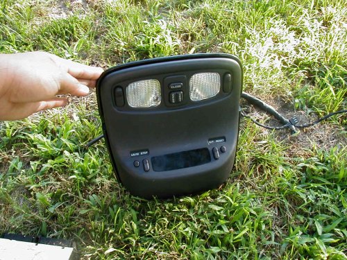 Black overhead dome light console with dual map lamps held over grass