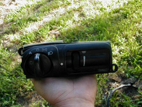 Hand holding black car headlight switch panel outdoors over grass
