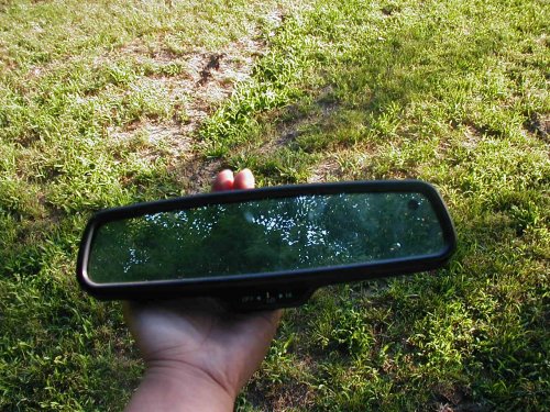 Hand holding a black automotive rear-view mirror over grass