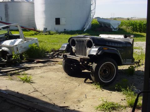 1992 Ford Bronco - A black Jeep CJ-7 Laredo sits in a yard next to a white Suzuki Samurai, with silos in the background.