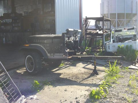 1992 Ford Bronco - A dark green Jeep CJ-7 is disassembled and supported by jack stands in an outdoor workshop area.
