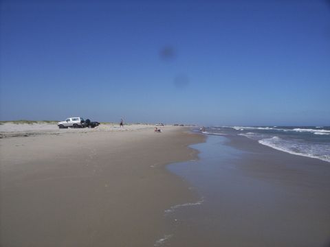 1995 Ford Bronco - A white SUV tows a trailer across a beach with the ocean nearby.