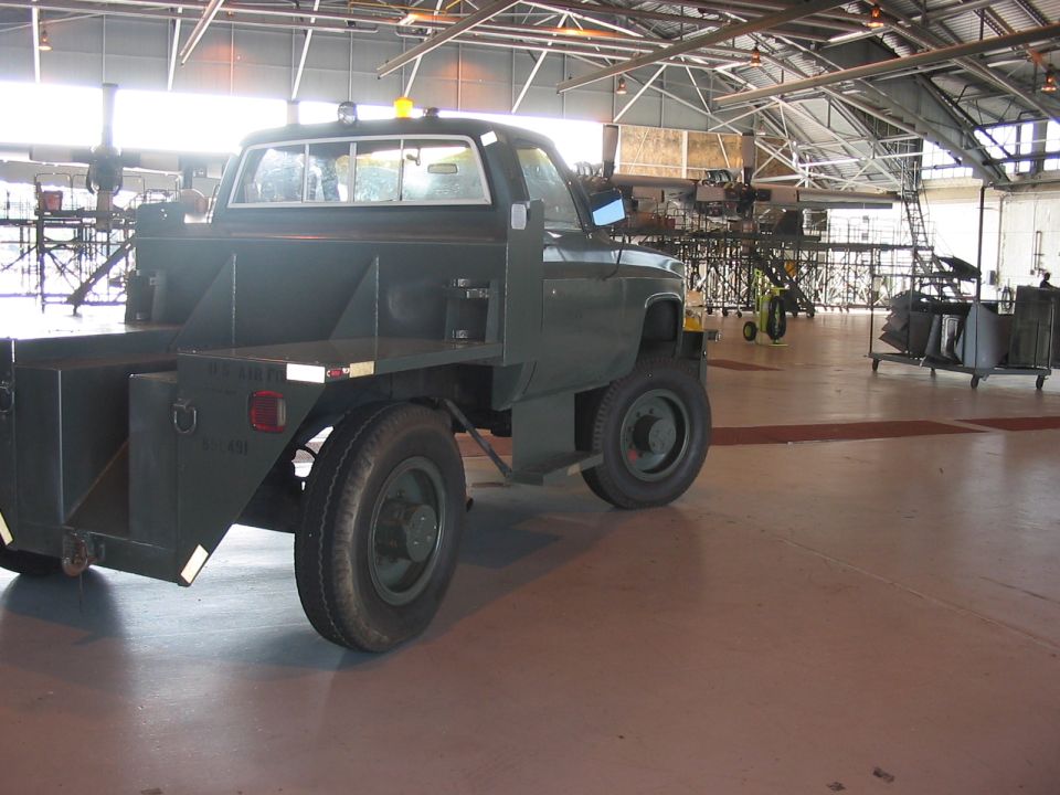 Green utility truck with a flatbed and toolboxes parked inside a large building