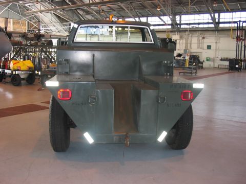 1988 Ford Bronco - This military truck has a flatbed rear and is parked inside a hangar.
