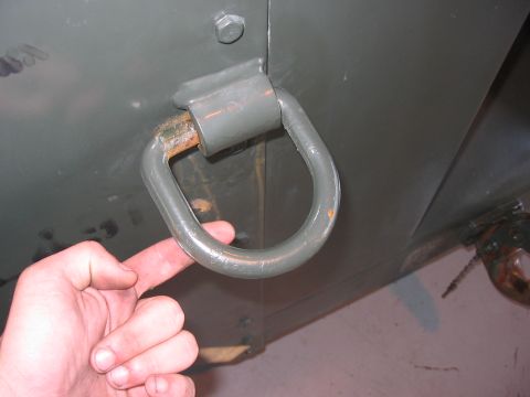 1988 Ford Bronco - A hand points to a rusty tow hook attached to the side of a utilitarian vehicle.