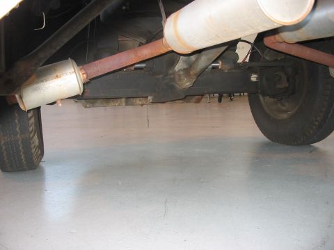 1988 Ford Bronco - The underside of a vehicle is visible, a rusty exhaust system and rear axle components.