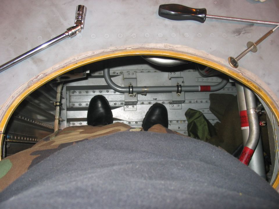 View from inside an aircraft looking down at feet and tools. Camouflage fabric is in the foreground