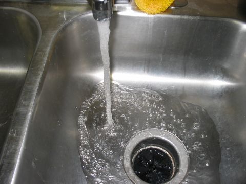 1988 Ford Bronco - Water flows into a stainless steel kitchen sink, filling the basin and going down the drain.