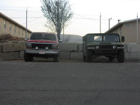 1981 Ford Bronco - Two distinct vehicles, a red Ford truck and a green Humvee, are parked side-by-side.