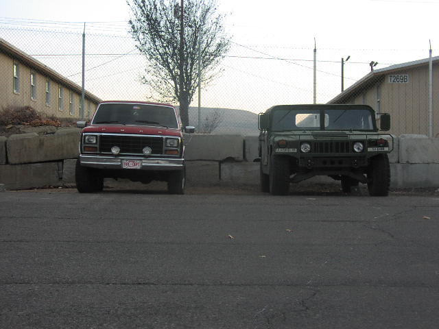 Red 1980s Ford F-Series truck parked next to a green Humvee