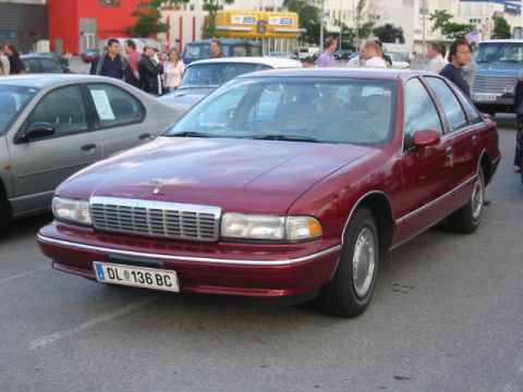1992 Ford Crown Victoria - A maroon sedan is parked in a lot with other vehicles and people around.