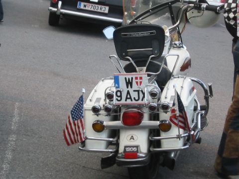 1992 Ford Crown Victoria - A white motorcycle with American flags and Austrian plates is seen from the rear, with another vehicle in the background.