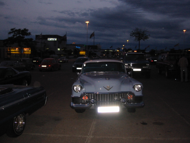 Light blue 1950s Cadillac parked at dusk, with other cars around