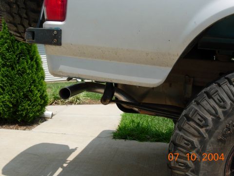 1995 Ford Bronco - A close-up view of the rear of a white SUV, focusing on the tire, exhaust, and body panel.