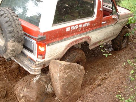 1985 Ford Bronco - This off-road vehicle is navigating a difficult terrain with large rocks and mud.