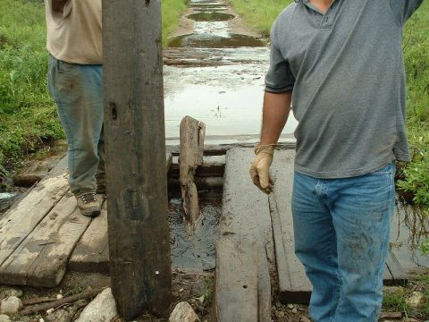 1985 Ford Bronco - Two men stand on a rustic wooden walkway crossing a muddy, waterlogged path.