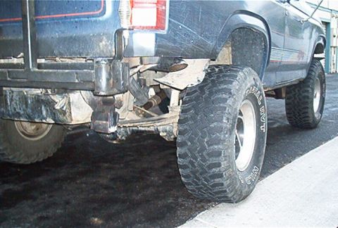 1986 Ford Bronco - Close-up view of the rear axle, leaf springs, and tires on a modified truck.