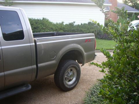 1995 Ford Bronco - A tan Ford F-250 Super Duty pickup truck is parked on a driveway next to a house and some bushes.