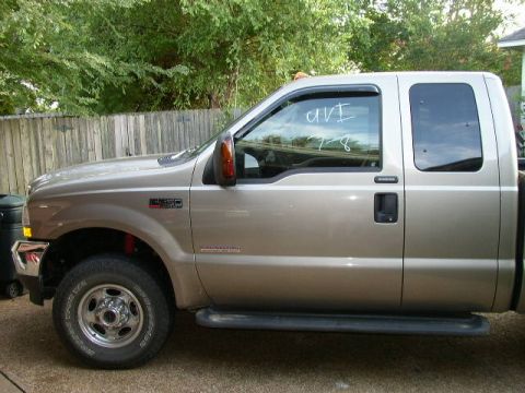 1995 Ford Bronco - Side view of a tan crew cab pickup truck with writing on the driver's side window.