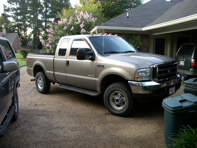 Tan Ford F-250 Super Duty pickup truck parked in driveway next to a dark SUV