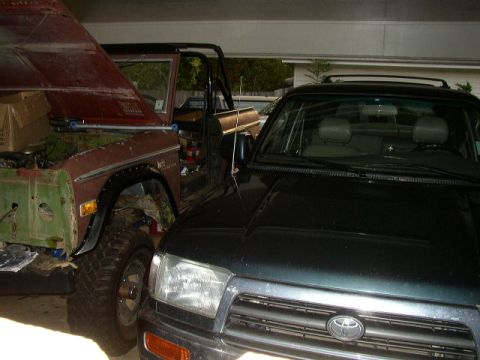 1995 Ford Bronco - A vintage Ford Bronco, appearing to be undergoing restoration, is parked next to a dark-colored SUV in a garage.