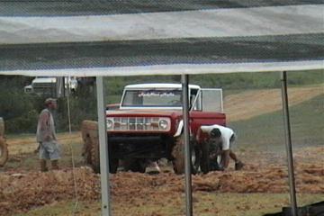 1989 Ford Bronco - A red Ford Bronco is being worked on in a muddy area, possibly during a mud bogging event.