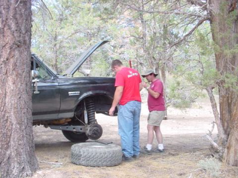 1988 Ford Bronco - Two men work on a 1988 Ford Bronco, which has its front wheel removed and hood up.