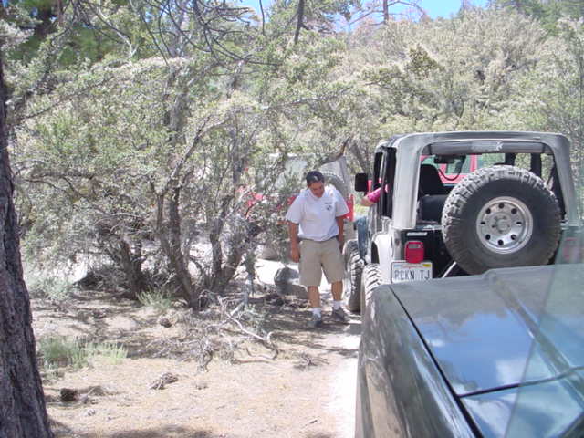 Man standing next to a Jeep Wrangler with a spare tire on the back. Another vehicle is in the foreground