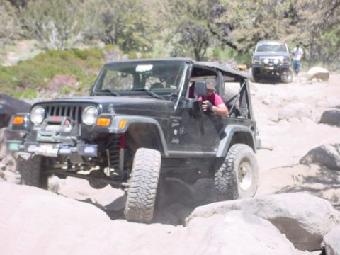 1988 Ford Bronco - A black Jeep Wrangler TJ is shown off-roading on a rocky trail, with another SUV visible in the background.