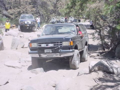 1988 Ford Bronco - Two Ford Broncos tackle a challenging rocky trail in a wooded area.