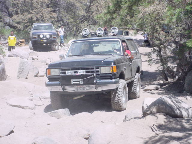 1987 Ford Bronco navigating a rocky off-road trail with another Bronco behind it