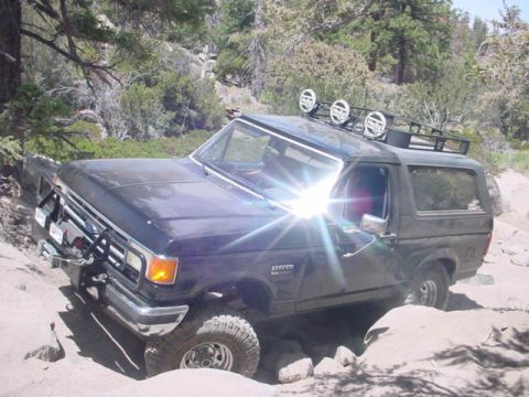 1988 Ford Bronco - A dark blue Ford Bronco is shown off-roading through a challenging rocky landscape.