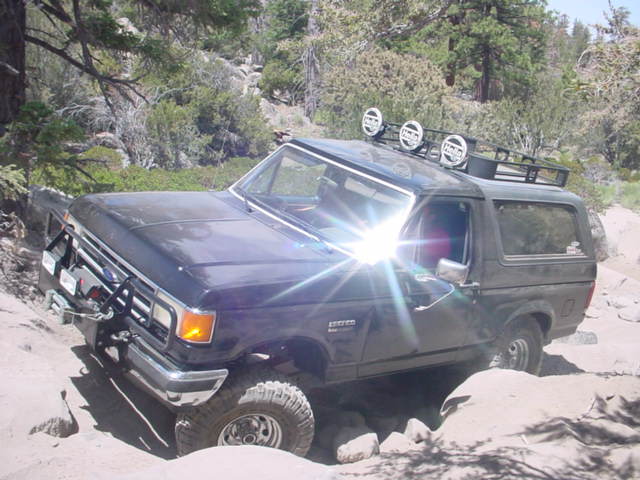 Dark blue Ford Bronco with a roof rack and off-road lights navigating a rocky terrain