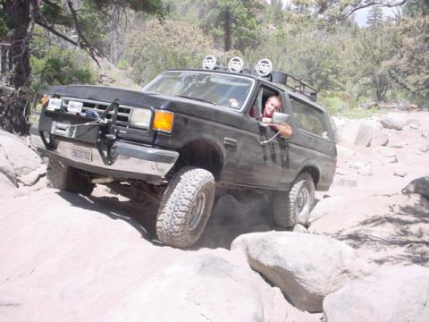 1988 Ford Bronco - A black 1988 Ford Bronco tackles a challenging rocky terrain, demonstrating its off-road capabilities.