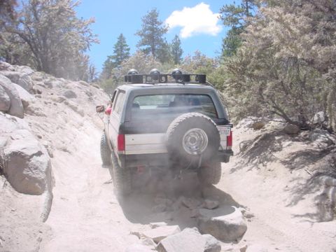 1988 Ford Bronco - A Ford Bronco navigates a challenging off-road path, kicking up dust.